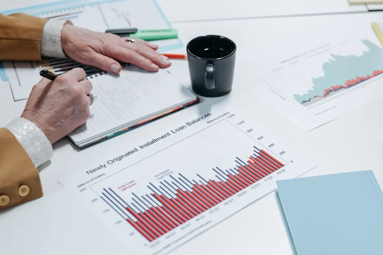 Hands reviewing printed financial charts and taking notes.
