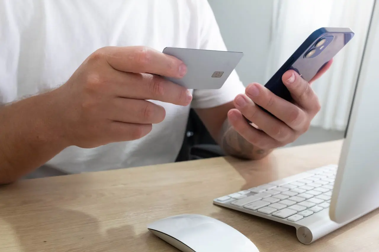 A person holding a payment card and smartphone at a desk.